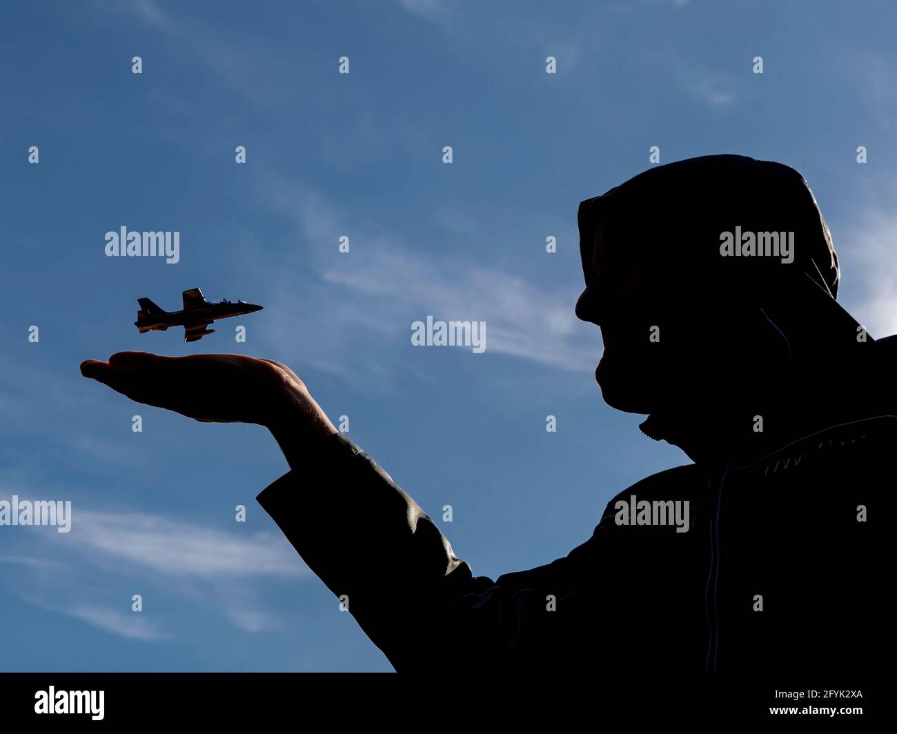 Silhouette di un uomo con cappuccio che ha un aereo che vola sopra la sua mano aperta contro un bel cielo blu Foto Stock