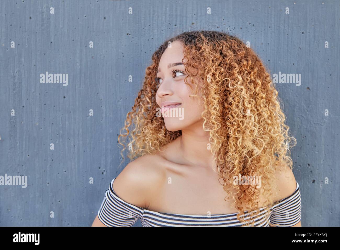 Ritratto sorridente di Latina teenager su sfondo grigio. Primo piano di giovane ragazza con capelli ricci felici. Foto di alta qualità Foto Stock