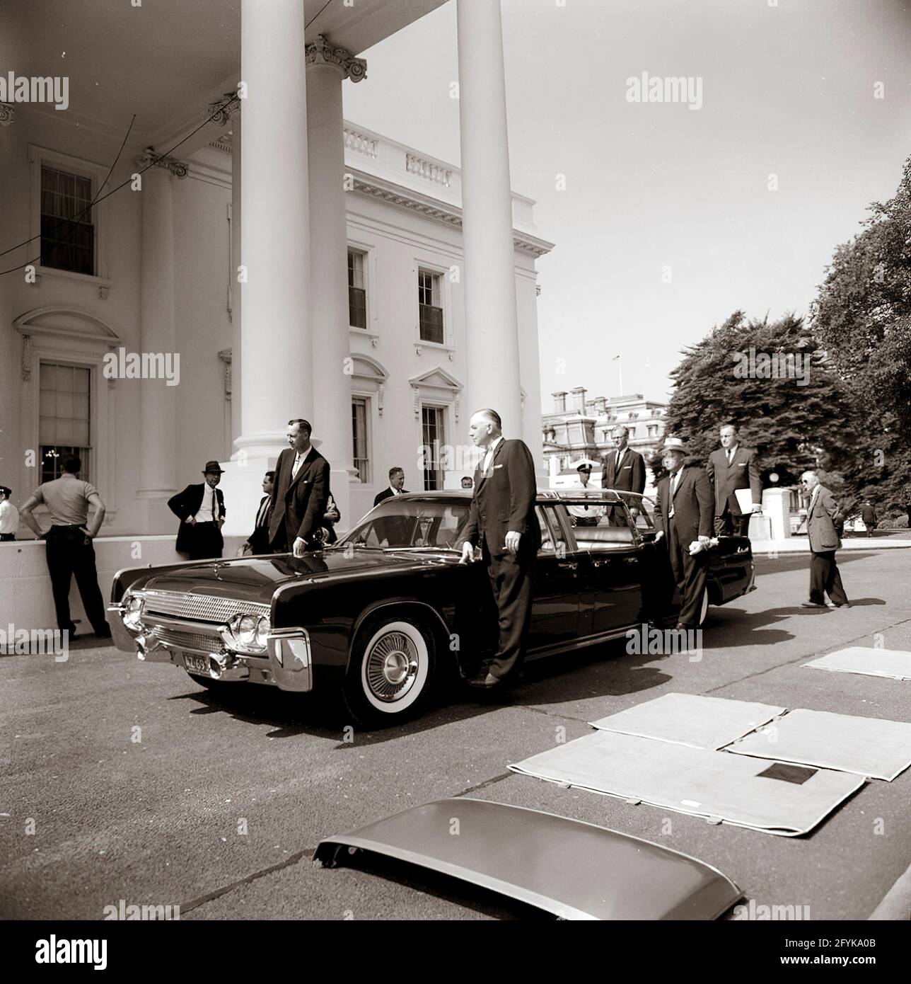 Arrivo della nuova limousine presidenziale (Lincoln-Mercury Continental convertibile con una bolla-top), costruita dalla Ford Motor Company e personalizzata da Hess & Eisenhardt. Il direttore del servizio segreto degli Stati Uniti, U. E. Baughman, e il fotografo DELLA RIVISTA LOOK, Stanley Tretick, si trovano a sinistra. Ford Motor Company ufficiale di collegamento alla Casa Bianca, Vaughn Ferguson, si trova sul cavalletto di auto lato conducente; altri in piedi sui lati e paraurti posteriore dell'automobile non sono identificati. Portico Nord, Casa Bianca, Washington, D.C. Foto Stock