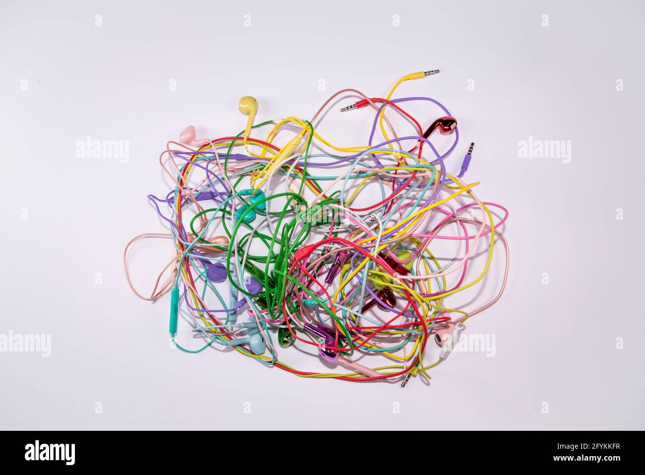 Auricolari multicolore aggrovigliati su fondo piatto di superficie bianca. Idea musicale. Concetto di partito astratto e tecnologia minimo. Foto Stock