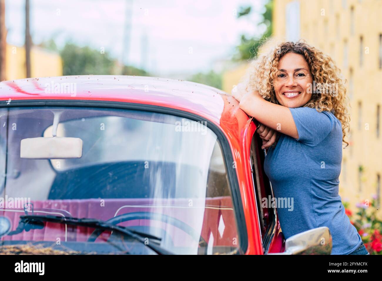 Ritratto di felice mezza età bella donna in piedi fuori di lei auto rossa classica e sorridente alla fotocamera - adulto donna godere di guida - gardon casa dentro Foto Stock
