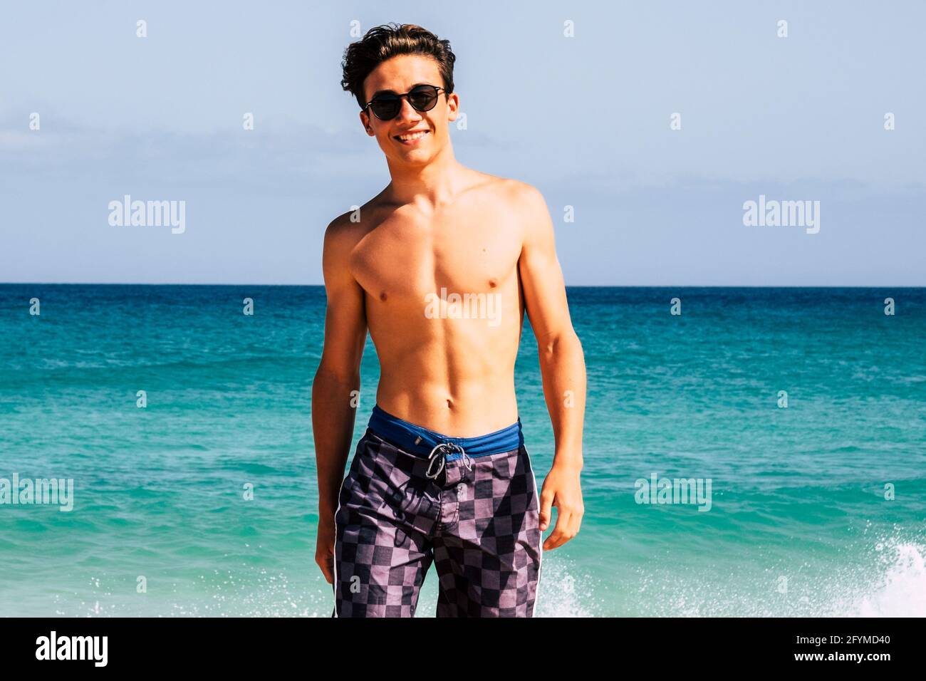 Giovane bel ragazzo in costume da bagno a piedi in spiaggia con cielo blu e  acqua dell'oceano sullo sfondo godendo l'estate all'aperto vacanza  sorridente Foto stock - Alamy