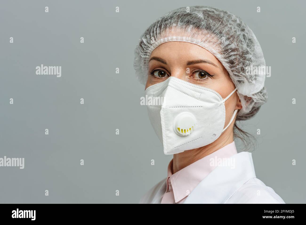 Ritratto di una giovane donna infelice medico in una maschera medica su sfondo grigio. Gli occhi stanchi del medico. Il concetto di coronavirus. Foto Stock