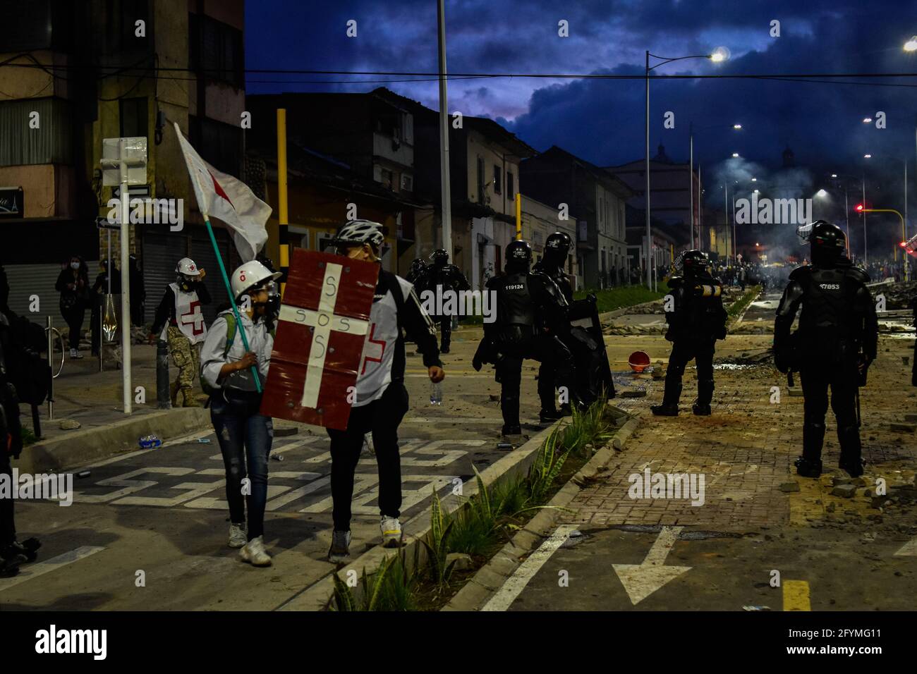 I membri delle missioni mediche usano scudi e bandiere per prevenire la violenza nei loro confronti durante gli scontri con la polizia antisommossa ESMAD mentre la Colombia segna il suo primo mese di proteste anti-governative contro la legge fiscale del Presidente Duque e le riforme sanitarie e la brutalità e i disordini della polizia, migliaia di persone inondano le strade di Pato, Narino, Colombia il 28 maggio 2021. Foto Stock