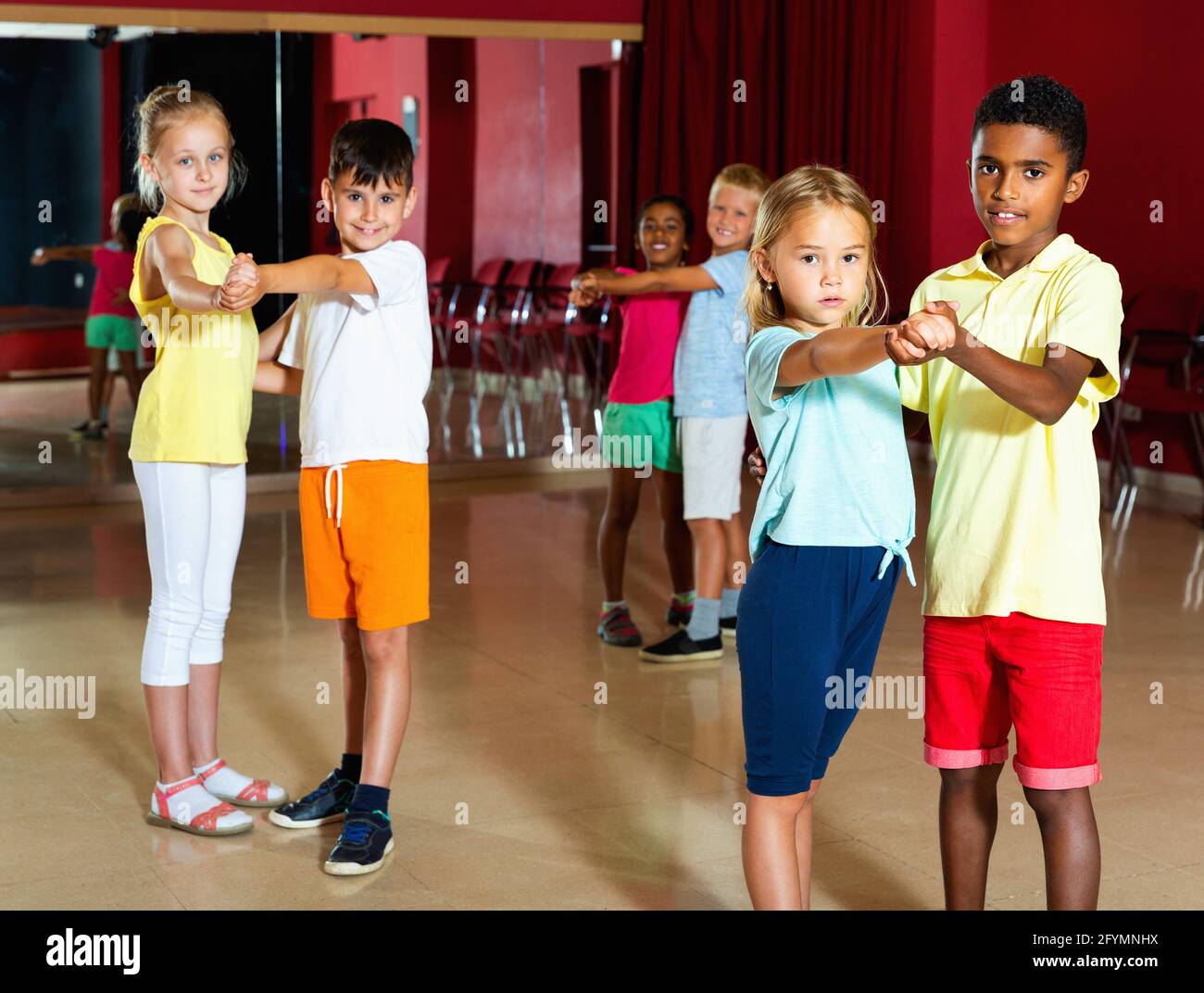 Gruppo di felici e allegri bambini sorridenti che cercano di ballare con il compagno in classe Foto Stock