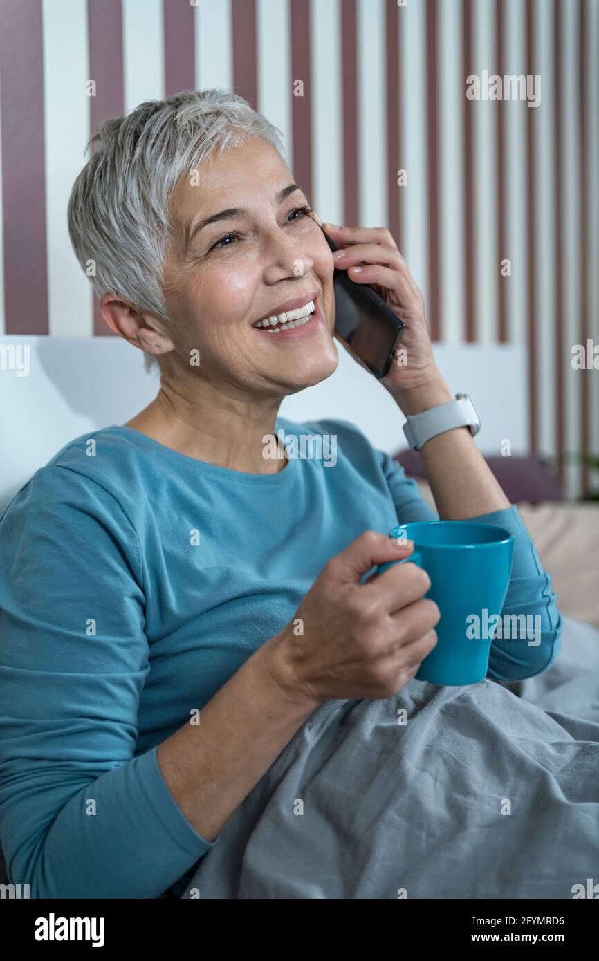 Donna che usa lo smartphone a letto Foto Stock
