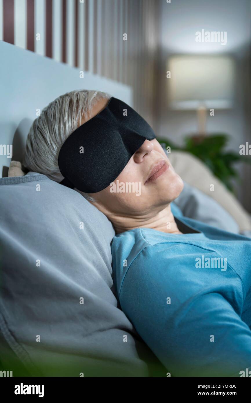 Donna matura che indossa la maschera nera del sonno Foto Stock