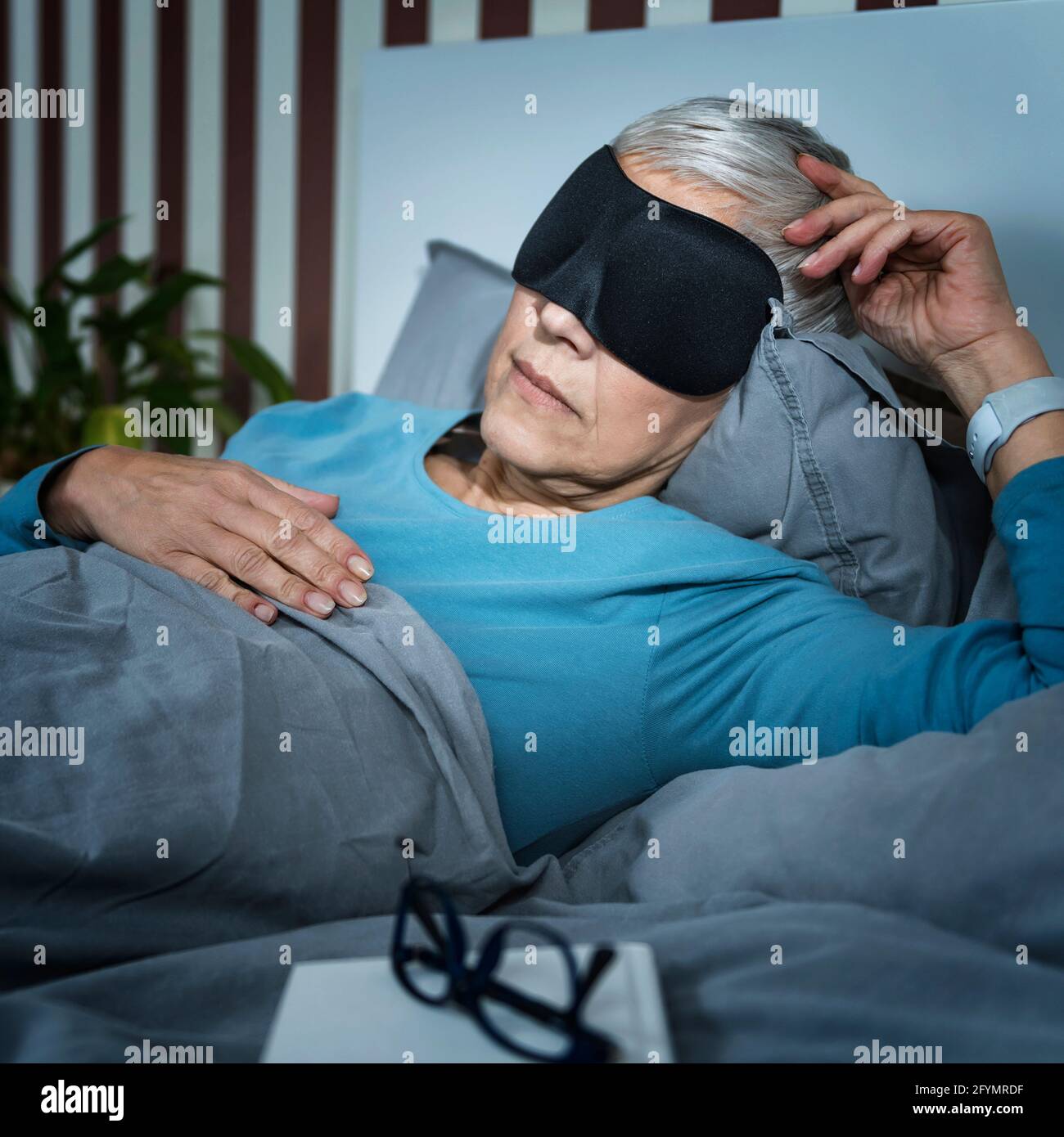 Donna matura che indossa la maschera nera del sonno Foto Stock