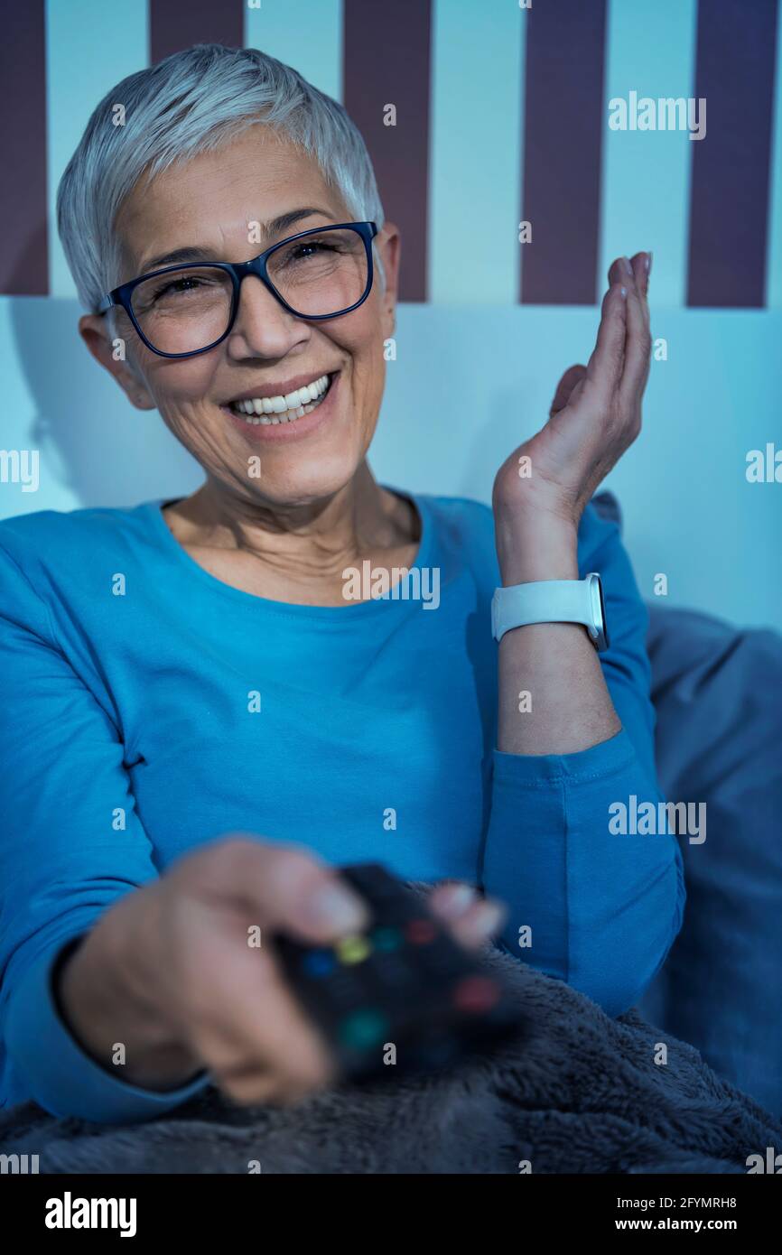 Donna anziana sorridente che guarda la televisione Foto Stock