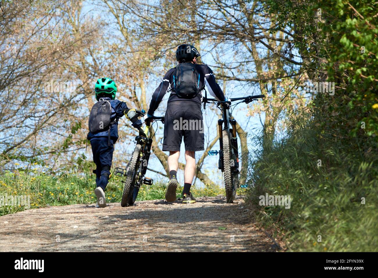padre aiuta suo figlio a spingere la bicicletta, in salita Foto Stock
