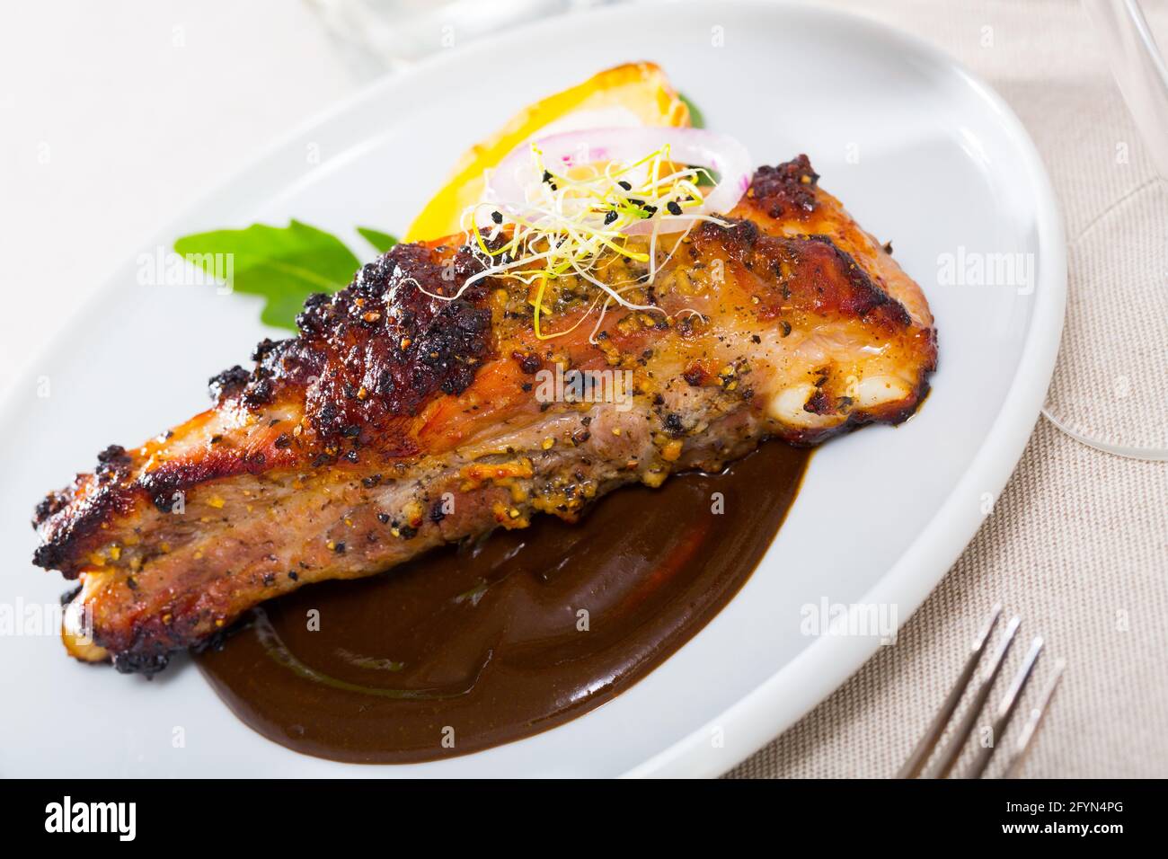 Costolette di maiale speziate arrostite servite su piatto bianco in salsa al cioccolato con patate e verdure al forno Foto Stock