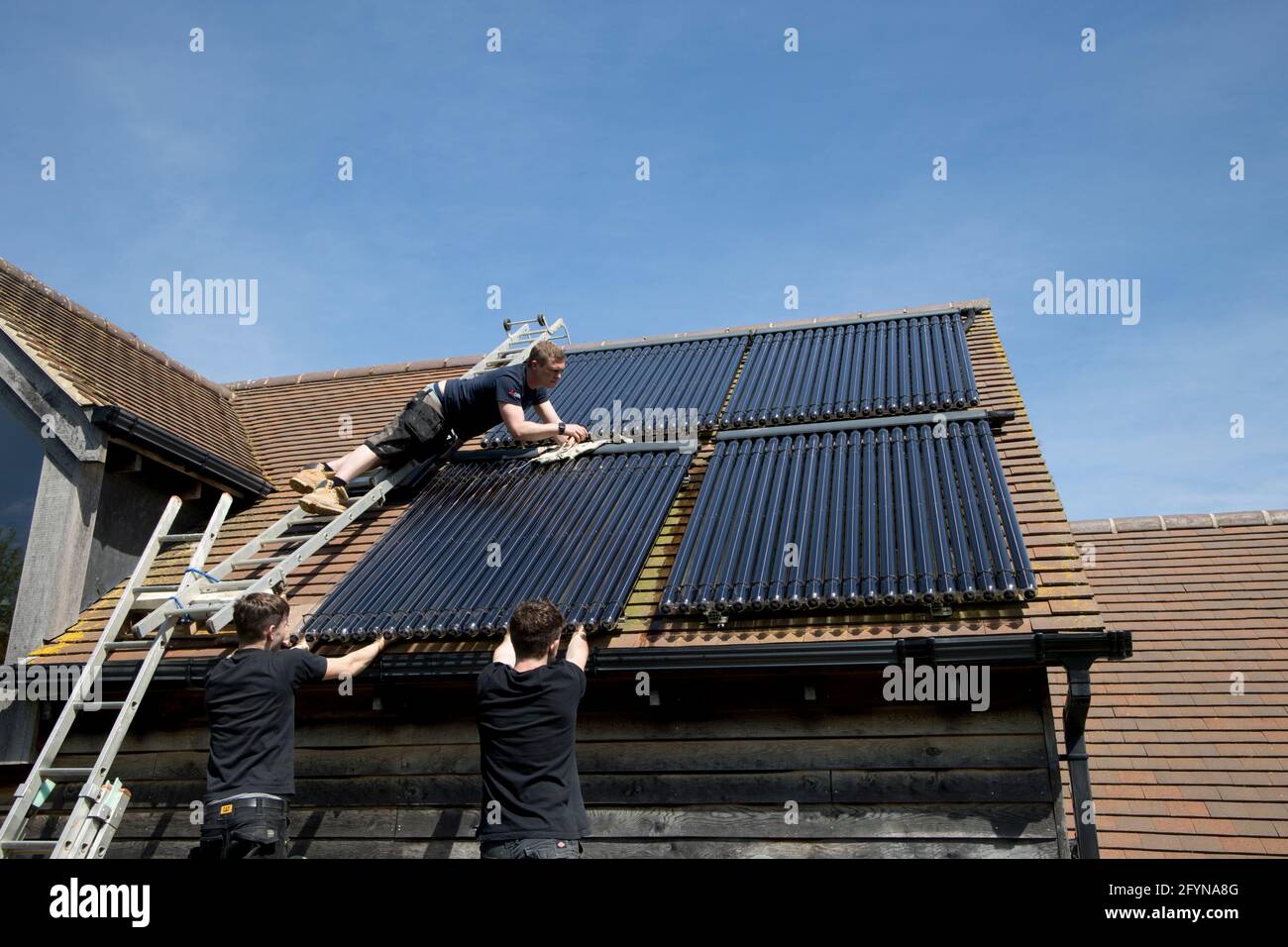 Ingegnere del riscaldamento che installa tubi di raccolta solare-termici evacuati a sud Di fronte al tetto di Ecofhouse in Cotswolds UK Foto Stock