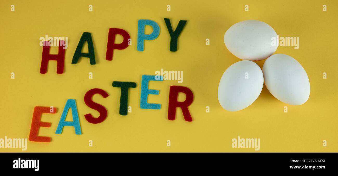 Buon biglietto d'auguri pasquale con tre uova bianche e colorate iscrizione su sfondo giallo Foto Stock
