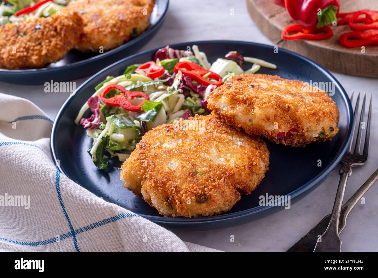 Deliziose torte di pesce in crosta di panko con insalata di cavolo e pepe rosso. Foto Stock