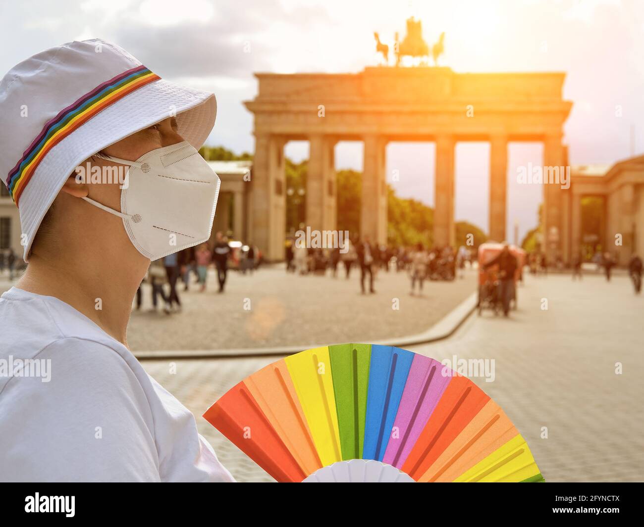 Donna LGBT caucasica matura a Berlino con ventola arcobaleno e nastro su cappello estivo bianco. Rainbow, simbolo dell'orgoglio gay LGBTQIA, la diversità. Donna che indossa Foto Stock
