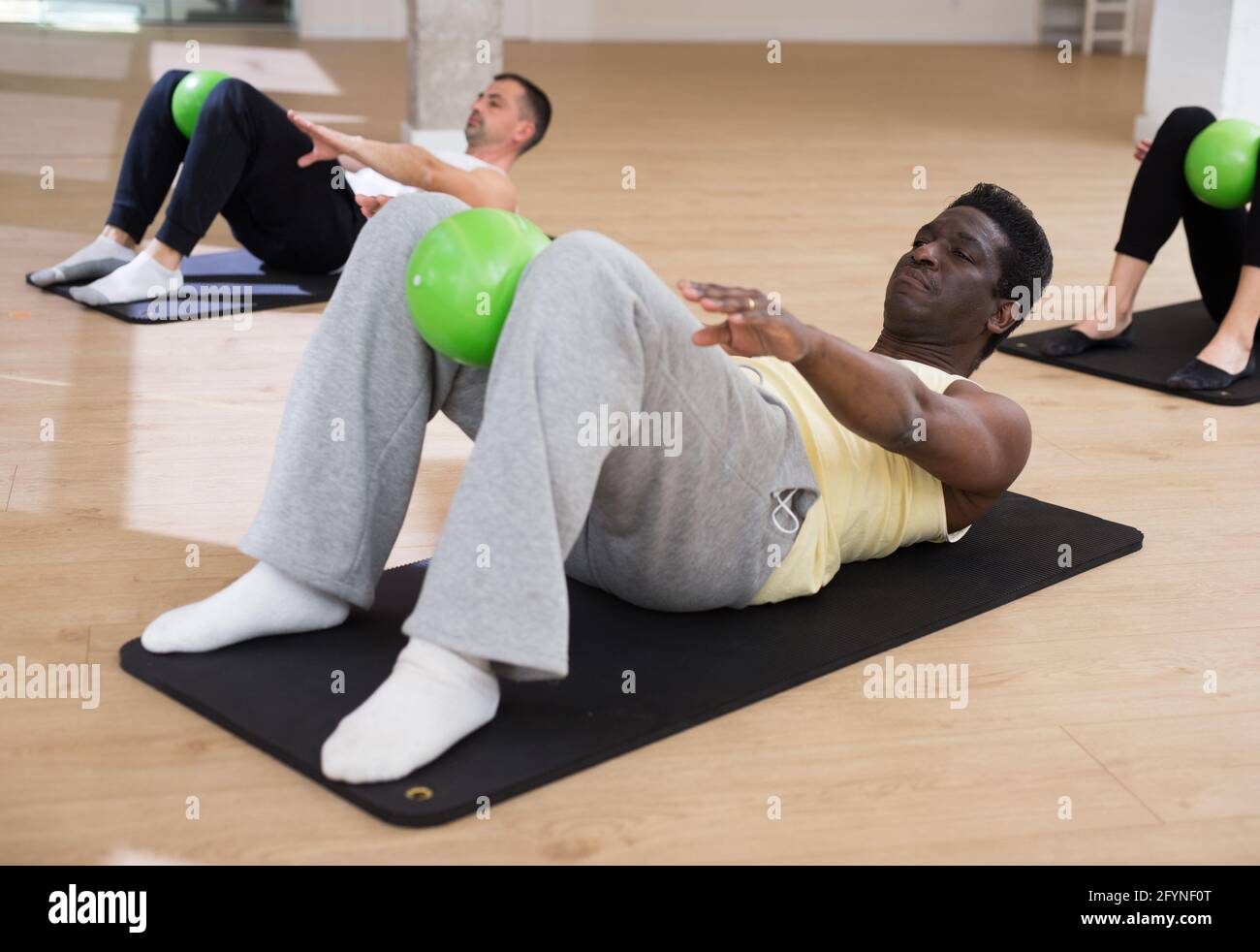 Concentrato afroamericano uomo esecuzione serie di esercizi abs con palla  bender durante la classe pilates di gruppo in studio fitness Foto stock -  Alamy