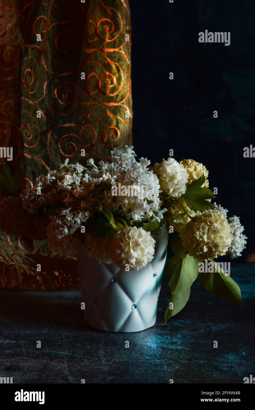 Composizione di un bouquet di fiori bianchi di viburno e lilla, in un contenitore bianco su sfondo scuro. Foto Stock