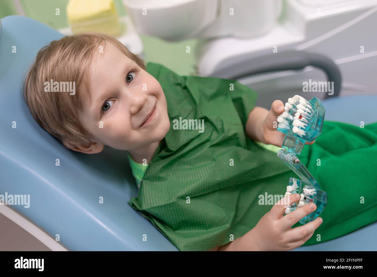 Sorriso capretto caucasico esamina i denti nella mascella sulla sedia al dentista, primo piano. Concetto per odontoiatria pediatrica, giochi e giocattoli in clinica. Foto Stock