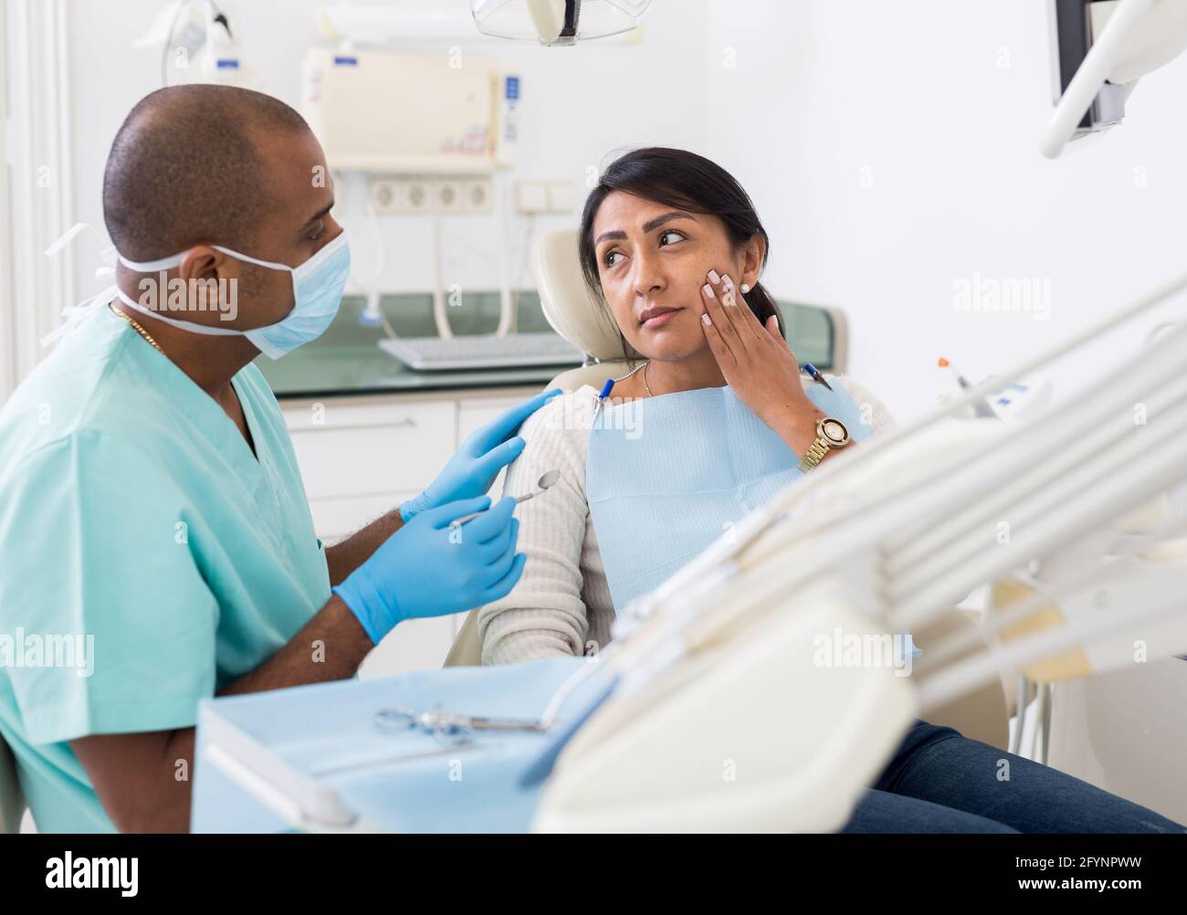 Turbata donna ispanica seduta in sedia dentale, lamentando a dentista qualificato circa il mal di denti Foto Stock