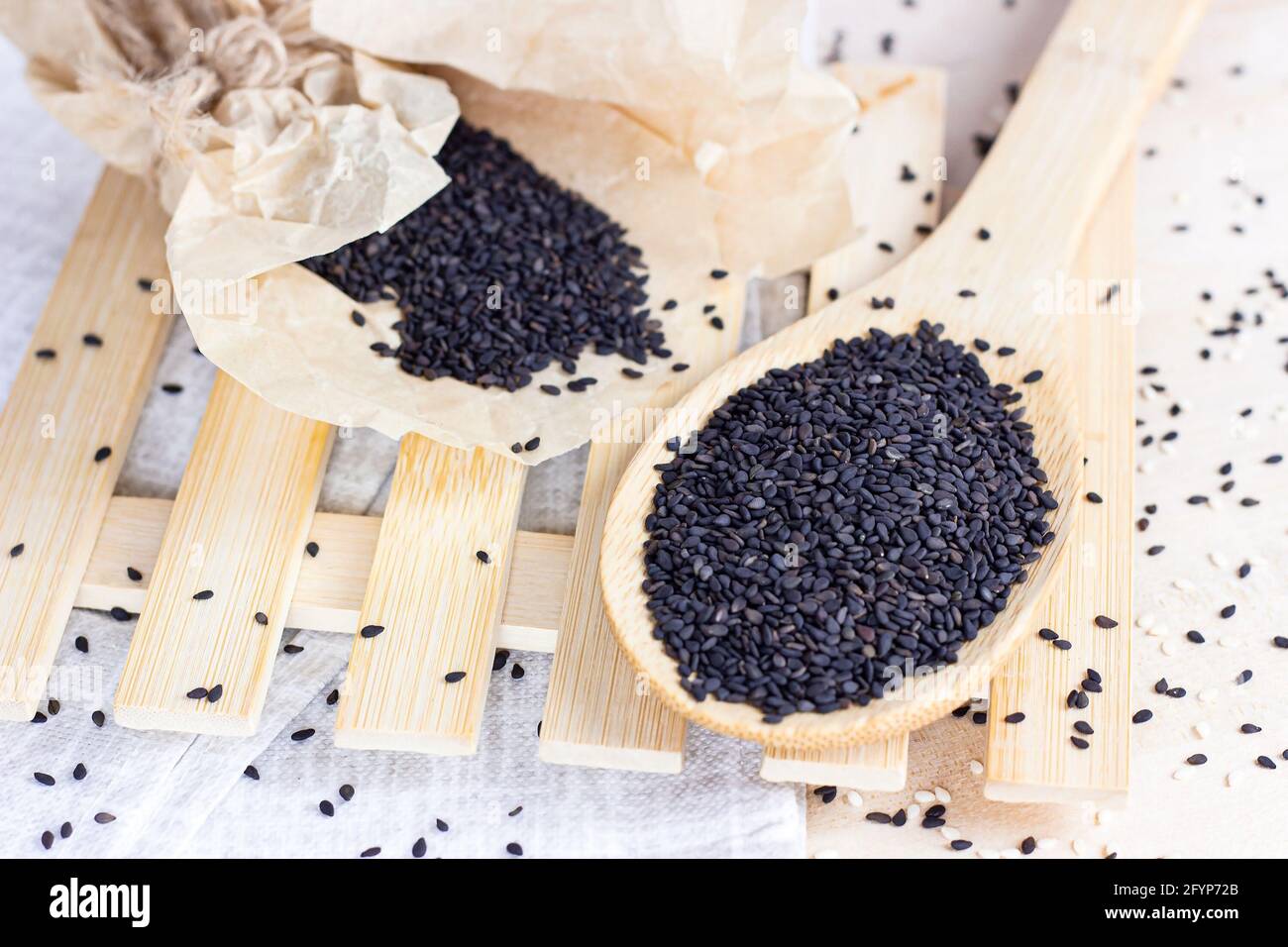 Semi di sesamo nero in un cucchiaio di legno per cucinare su sfondo chiaro in cucina. Foto Stock