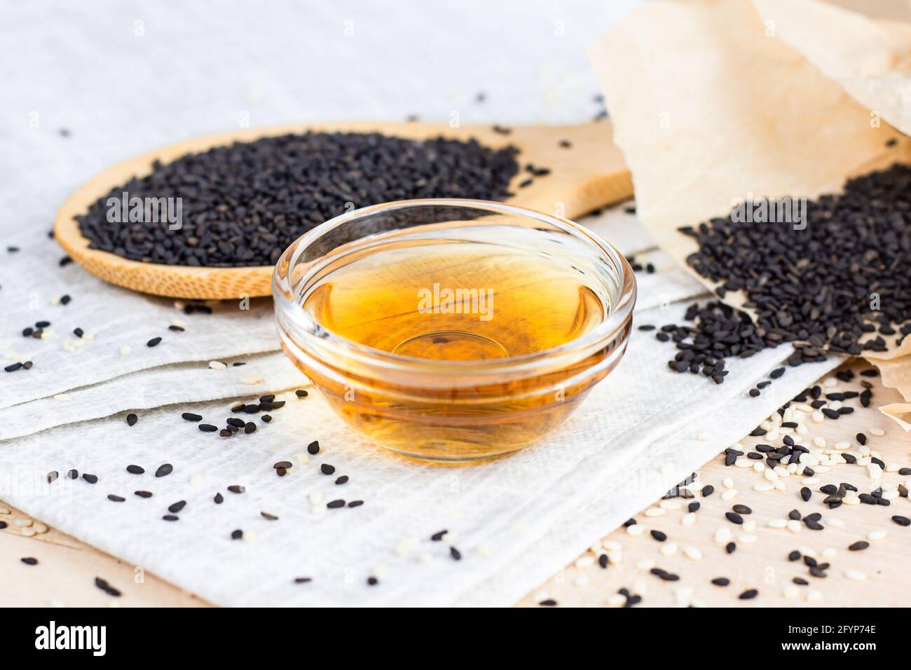 Semi di sesamo nero in un cucchiaio di legno e olio su sfondo chiaro in cucina. Foto Stock