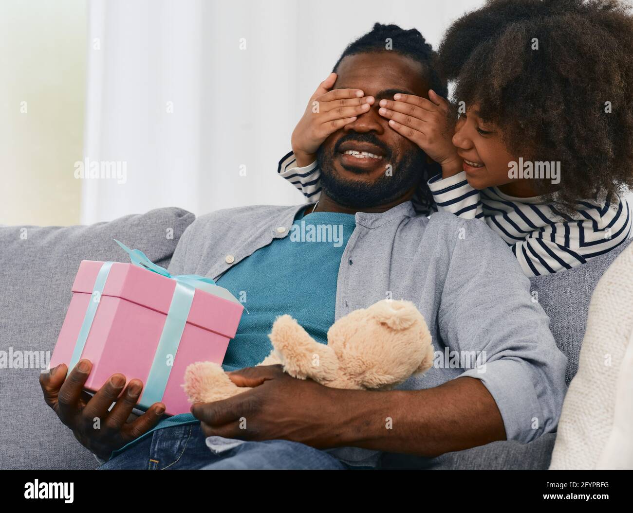La bambina afroamericana dona al papà un regalo per il giorno del papà. Sorpresa da figlia per padre Foto Stock