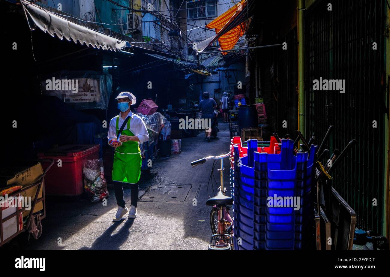 Un giovane operaio di ristorante maschile cammina lungo un vicolo illuminato dal sole a Chinatown, Bangkok, Thailandia Foto Stock