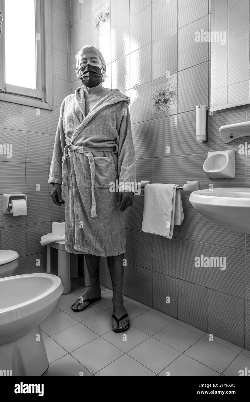 Uomo di mezza età in bagno, con accappatoio bianco e maschera protettiva Foto Stock