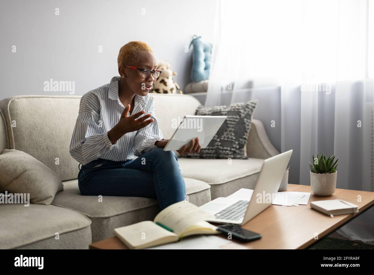 Donna d'affari nera che ha riunione in linea via tablet a casa Foto Stock