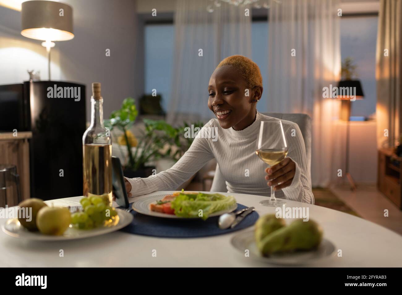 Felice donna nera che ha data in linea durante la cena a casa Foto Stock