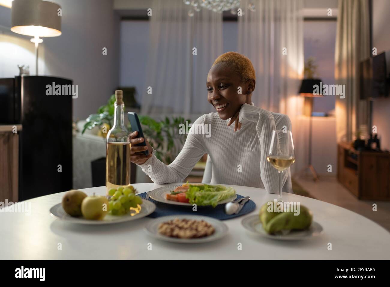 Giovane donna con cena e videochiamata su smartphone Foto Stock