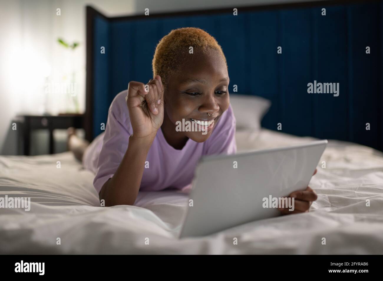 Donna felice sdraiata a letto e con videochiamata sul tablet Foto Stock