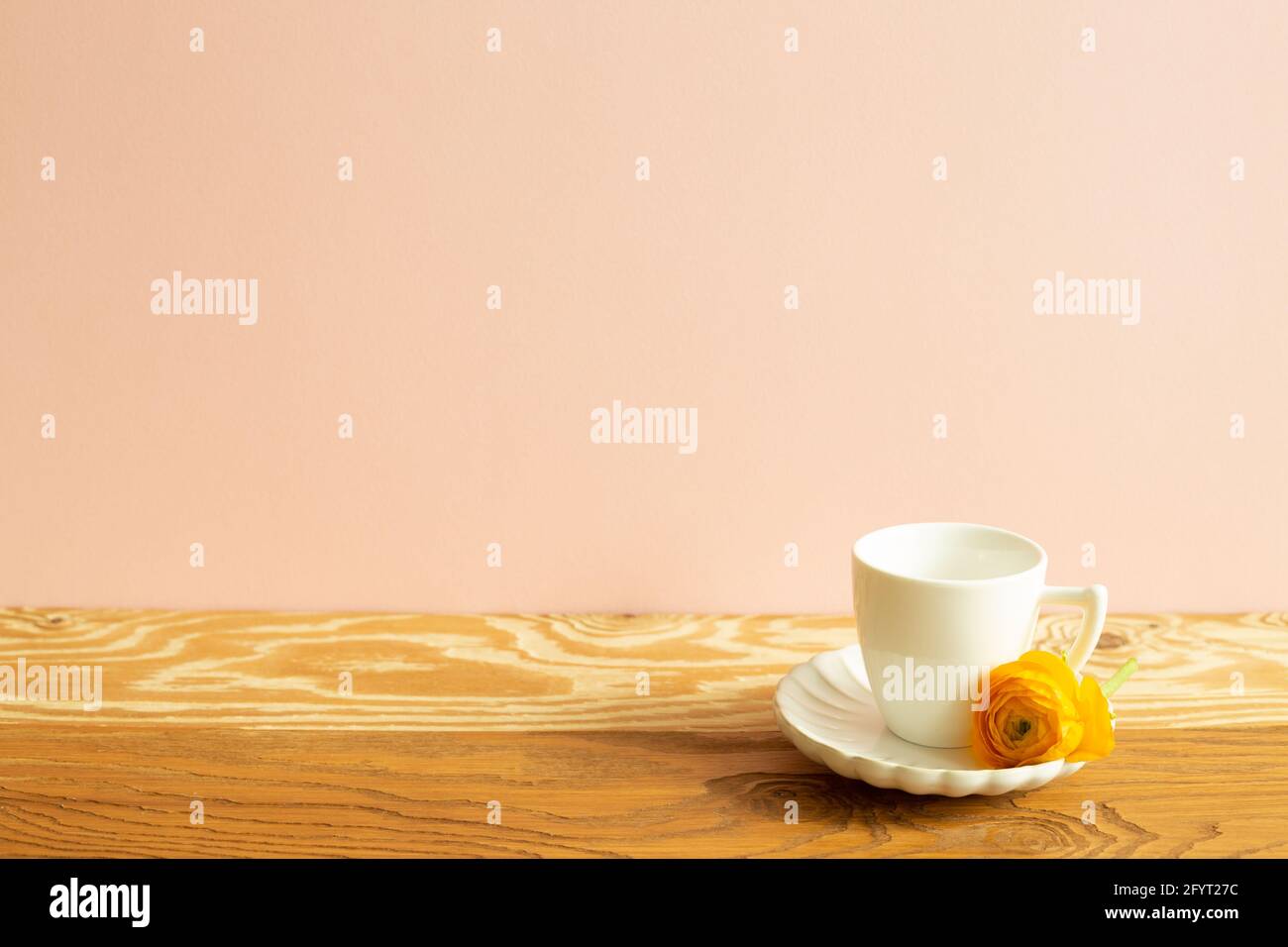 Tazza di caffè bianca con fiore giallo su tavolo di legno. Sfondo rosa Foto Stock