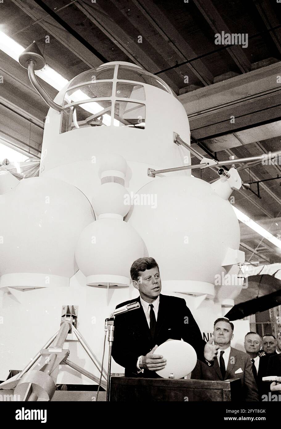 12 settembre 1962 il presidente John F. Kennedy (al leggio) fa commenti, dopo un tour delle mostre di veicoli spaziali all'interno di un hangar presso il Rich Building del presidiato Spacecraft Center, Houston, Texas. Il presidente Kennedy possiede un modello in scala del modulo di comando Apollo, presentato a lui dal direttore del presidiato Spacecraft Center, il dottor Robert Gilruth; un mock-up del lander lunare (noto anche come 'il Bug') si trova sullo sfondo. In piedi: Amministratore della National Aeronautics and Space Administration (NASA), Dr. James E. Webb; Governatore del Texas, Price Daniel; Direttore delle operazioni per Pr Foto Stock