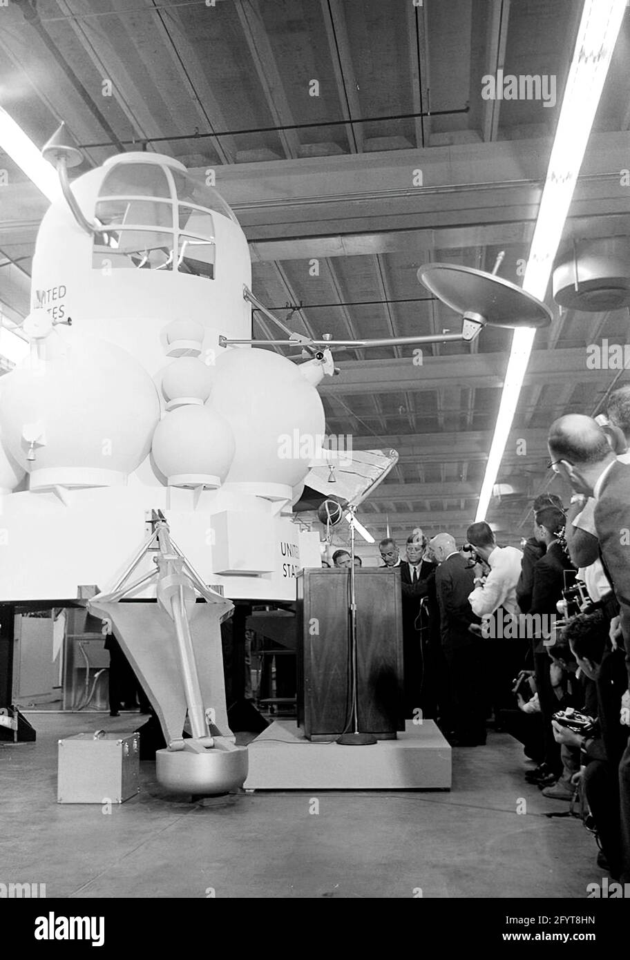12 settembre 1962 il presidente John F. Kennedy (al leggio) fa commenti, dopo un tour delle mostre di veicoli spaziali all'interno di un hangar presso il Rich Building del presidiato Spacecraft Center, Houston, Texas. Il presidente Kennedy possiede un modello in scala del modulo di comando Apollo, presentato a lui dal direttore del presidiato Spacecraft Center, il dottor Robert Gilruth; un mock-up del lander lunare (noto anche come 'il Bug') si trova sullo sfondo. In piedi: Amministratore della National Aeronautics and Space Administration (NASA), Dr. James E. Webb; Governatore del Texas, Price Daniel; Direttore delle operazioni per Pr Foto Stock