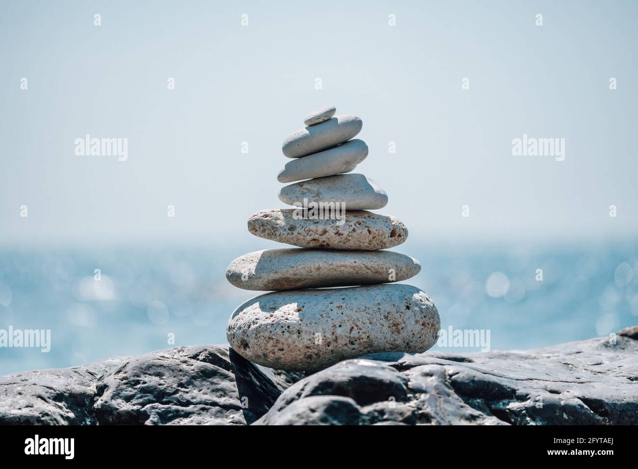 Equilibrata piramide di ciottoli sulla spiaggia in una giornata di sole. Abstract Sea bokeh sullo sfondo. Messa a fuoco selettiva. Pietre Zen sulla spiaggia di mare, meditazione Foto Stock