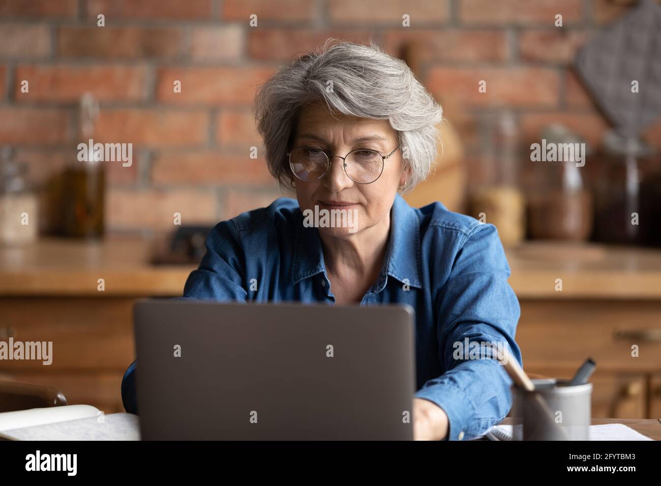 Donna seria che lavora su un computer portatile seduto al tavolo in cucina Foto Stock