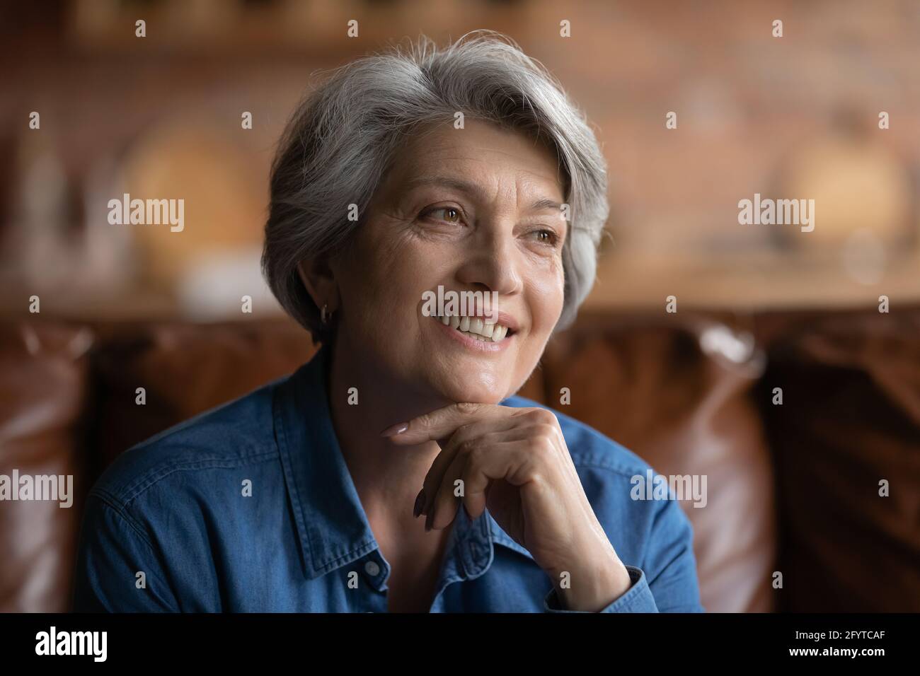 Anziana femmina in stolta seduta sul divano sorridente guardando via Foto Stock