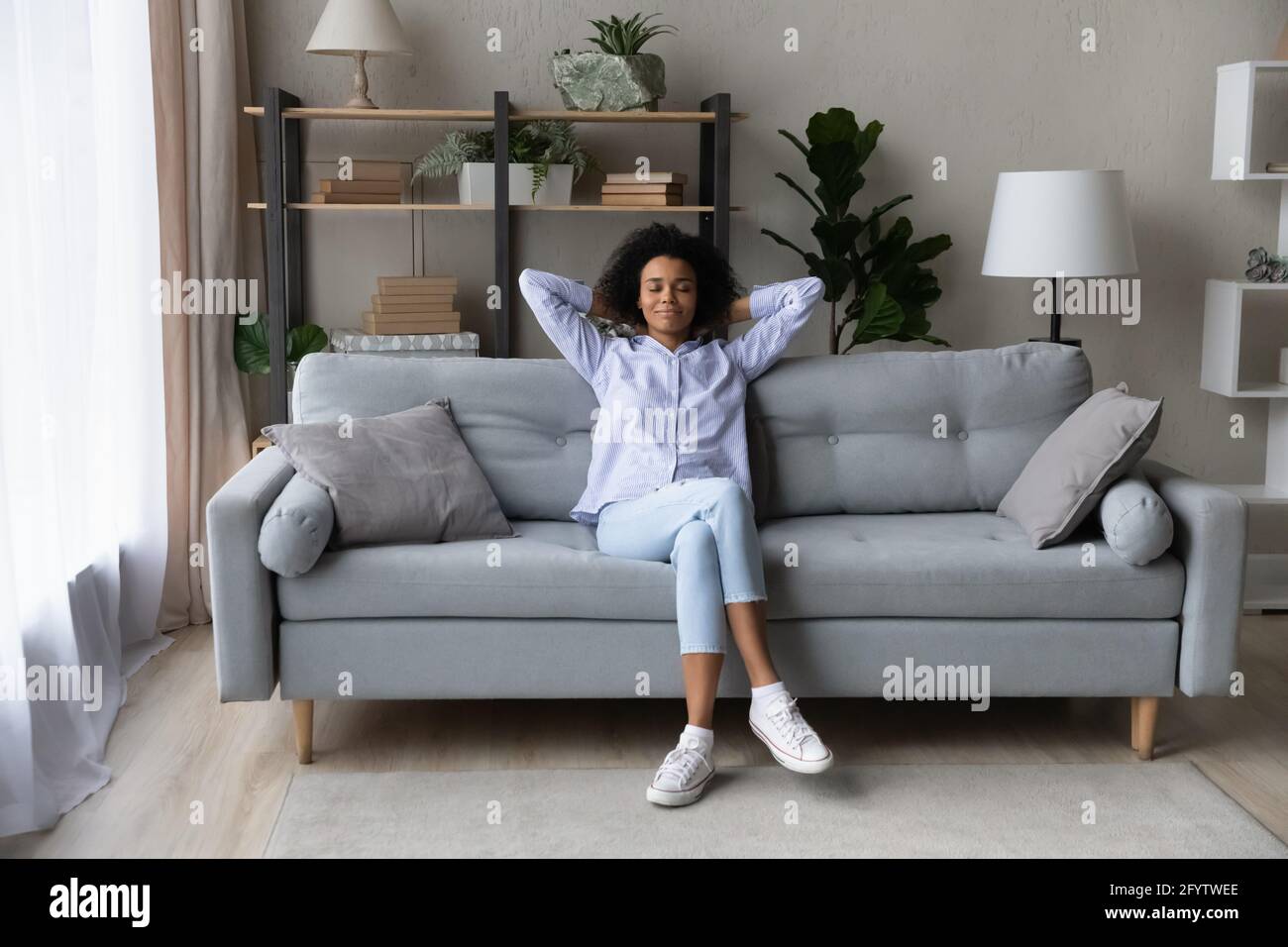 Donna afro-americana felice rilassarsi sul divano a casa Foto Stock