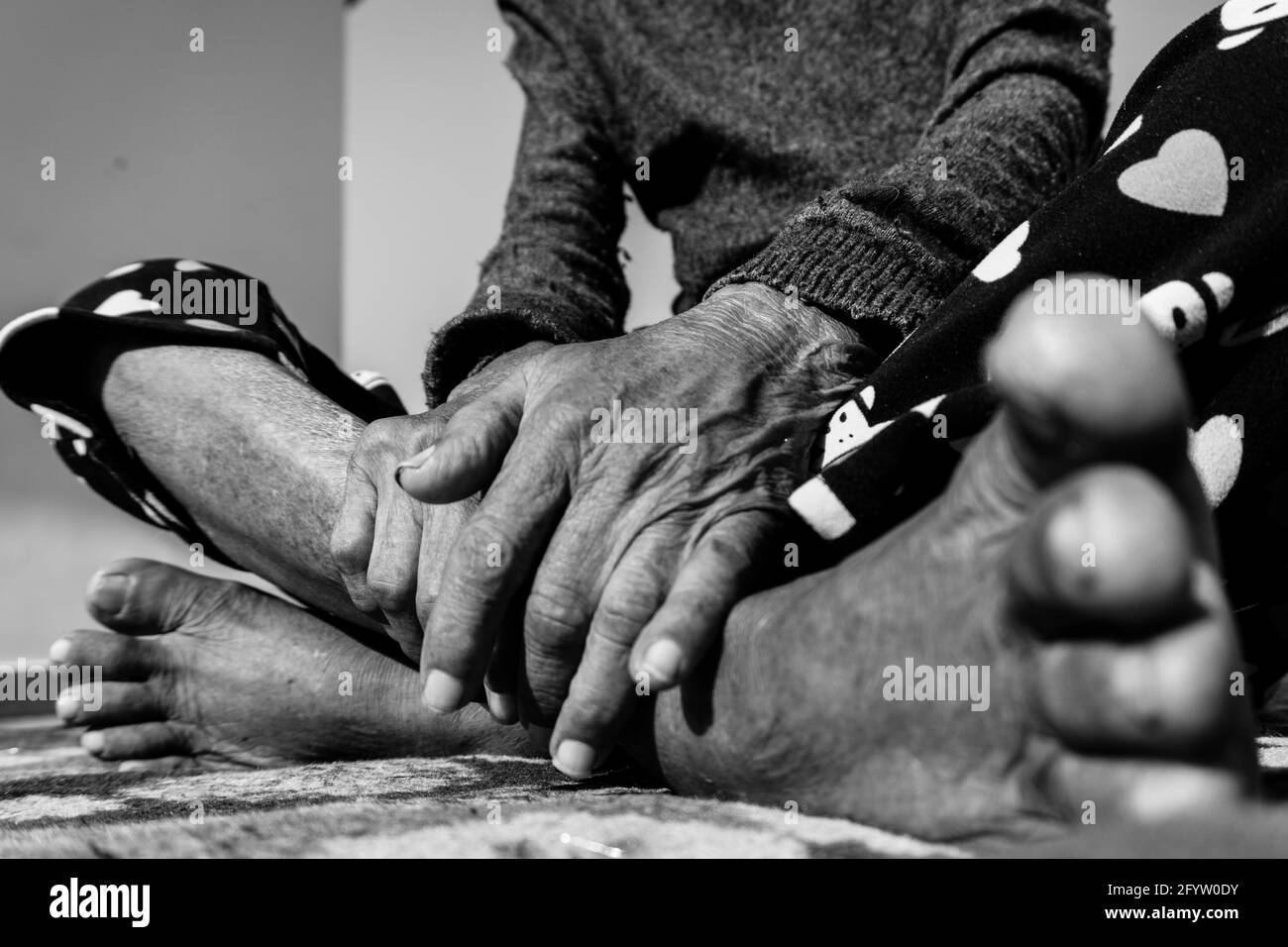 Un primo piano di piedi e mani di una donna anziana in India in bianco e nero. Foto Stock