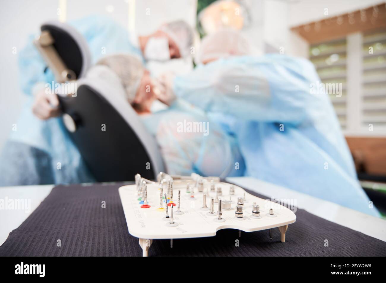 Immagine ravvicinata del set di teste metalliche per la macchina per la bur dentale aperto sul tavolo in primo piano, fuoco selettivo. Dentista durante l'intervento su sfondo sfocato. Concetto di trattamento Foto Stock
