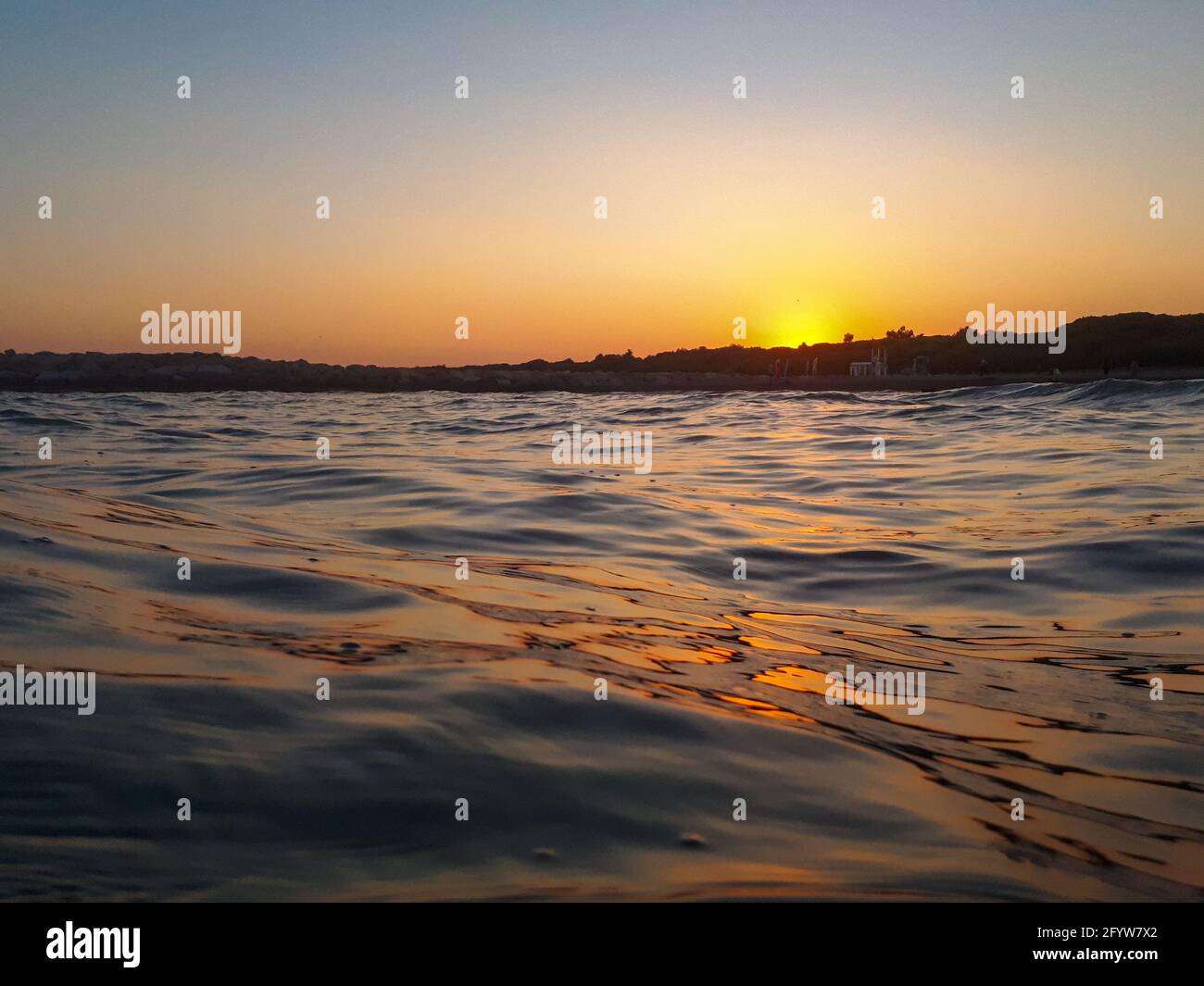 Ripresa del tramonto sul mare a livello della superficie, con una bella silhouette all'orizzonte Foto Stock