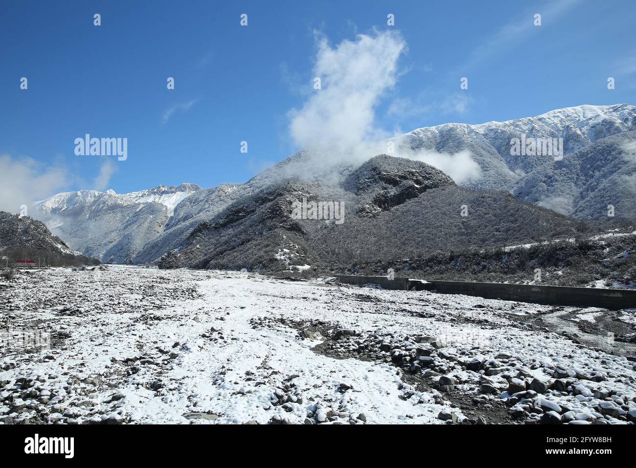 Ponte sul fiume. Inverno e montagna . C'è nebbia ai piedi delle montagne . Ha nevicato sulle pietre del fiume. In inverno, l'acqua del fiume è diminuita Foto Stock
