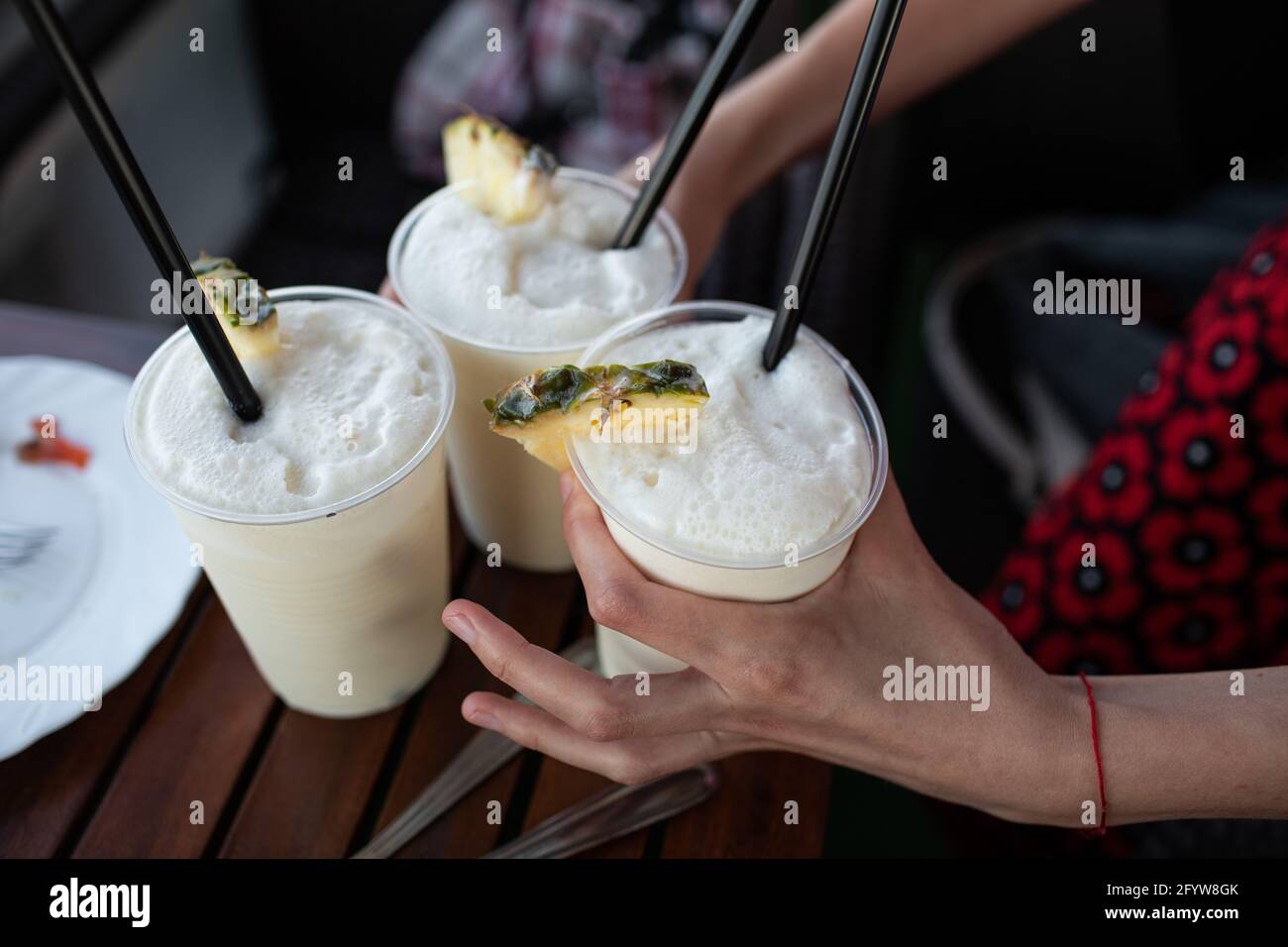Le mani della donna tengono tre cocktail in bicchieri di plastica con nero cannucce Foto Stock