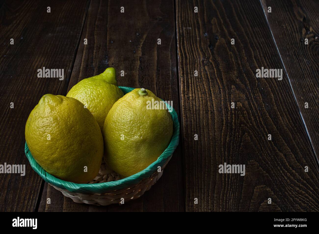 Un closeupshot di tre limoni interi in una ciotola sopra un tavolo di legno Foto Stock