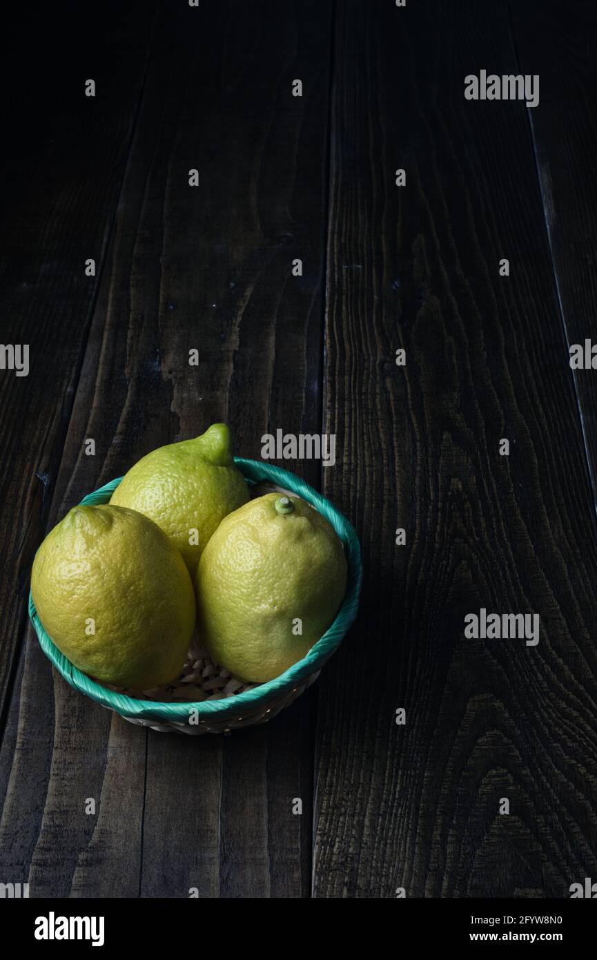 Un colpo verticale di tre limoni interi in una ciotola su un tavolo di legno Foto Stock