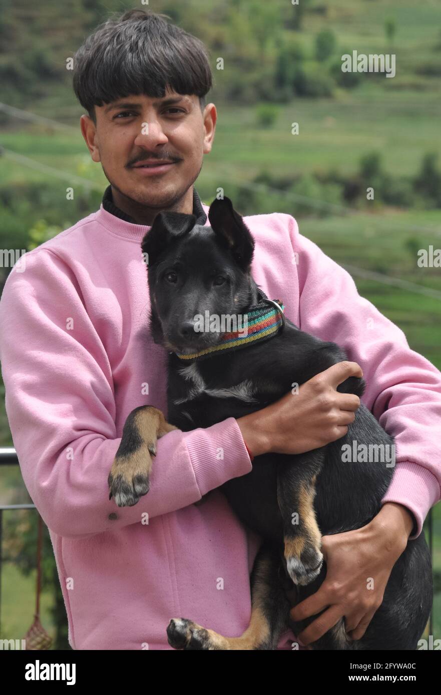 Vista frontale di un bel giovane ragazzo in piedi all'aperto con tenendo il cane di colore nero in mano Foto Stock