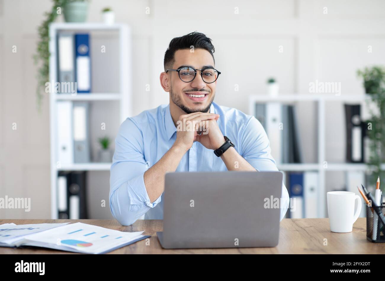 Ritratto di giovane arabo professionista seduto alla sua scrivania con un pc portatile in un ufficio moderno Foto Stock