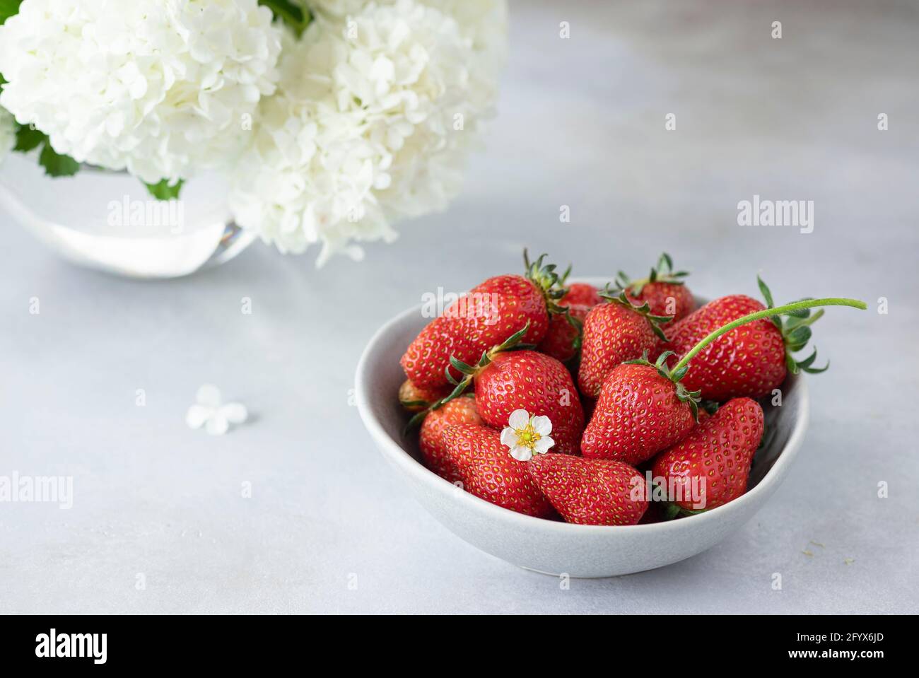 ciotola con fragole fresche e bel bouquet di fiori bianchi. sana alimentazione vitaminica. spazio copia. Sfondo grigio. Foto Stock