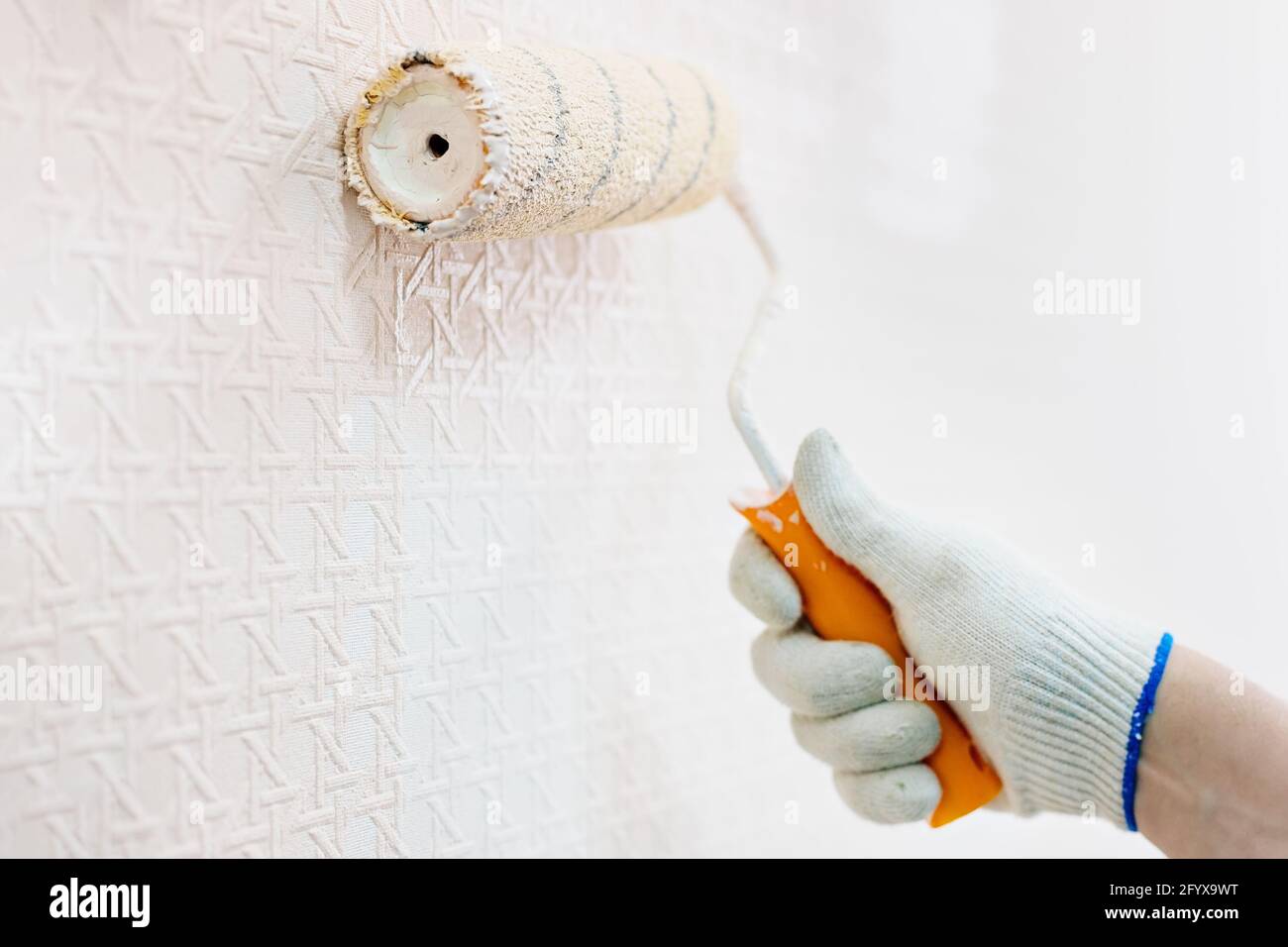 Una mano guanto e un rullo di vernice dipingono la parete in beige. Il concetto di ristrutturazione dei locali. Primo piano Foto Stock
